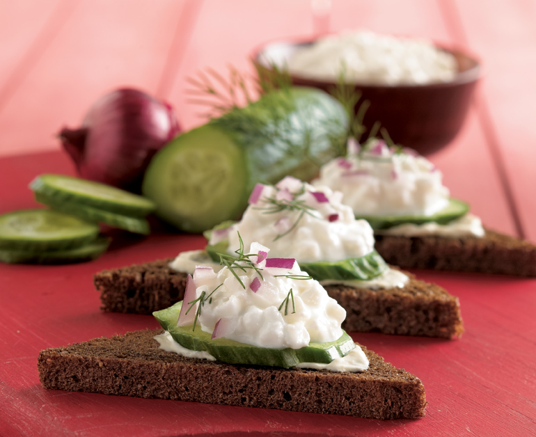 cucumber salad on rye toast points. A cucumber, shallot, and a bowl of dip are in the background.