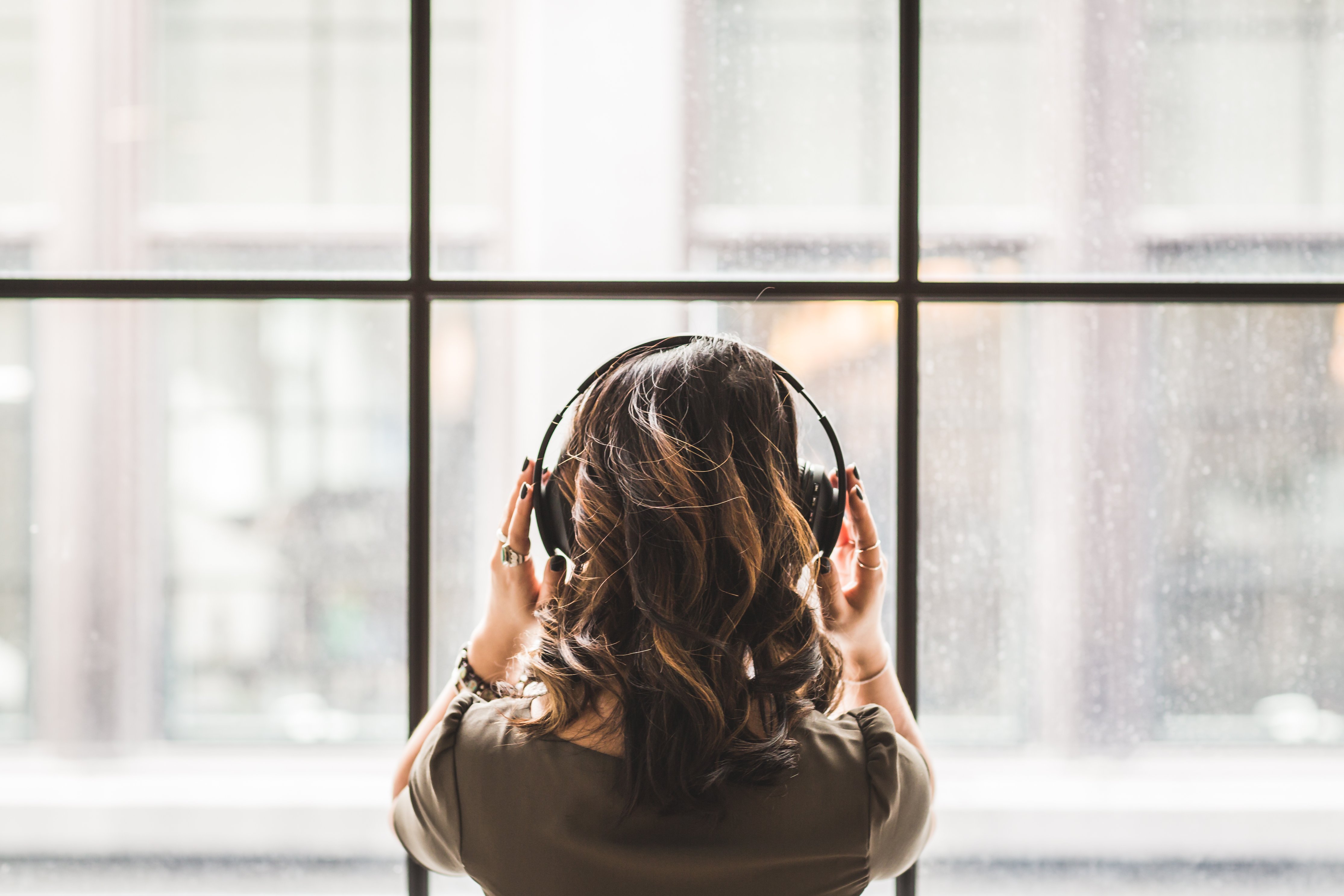 Woman wearing over-the-ear headphones looks out a window