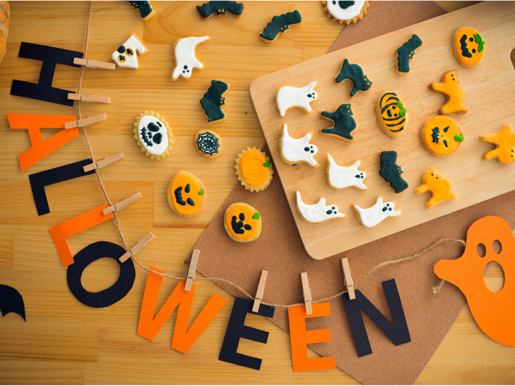 Halloween cookies of pumpkins, ghosts, cats accompany a twine string garland with the word HALLOWEEN spelled out in paper attached by clothespins.