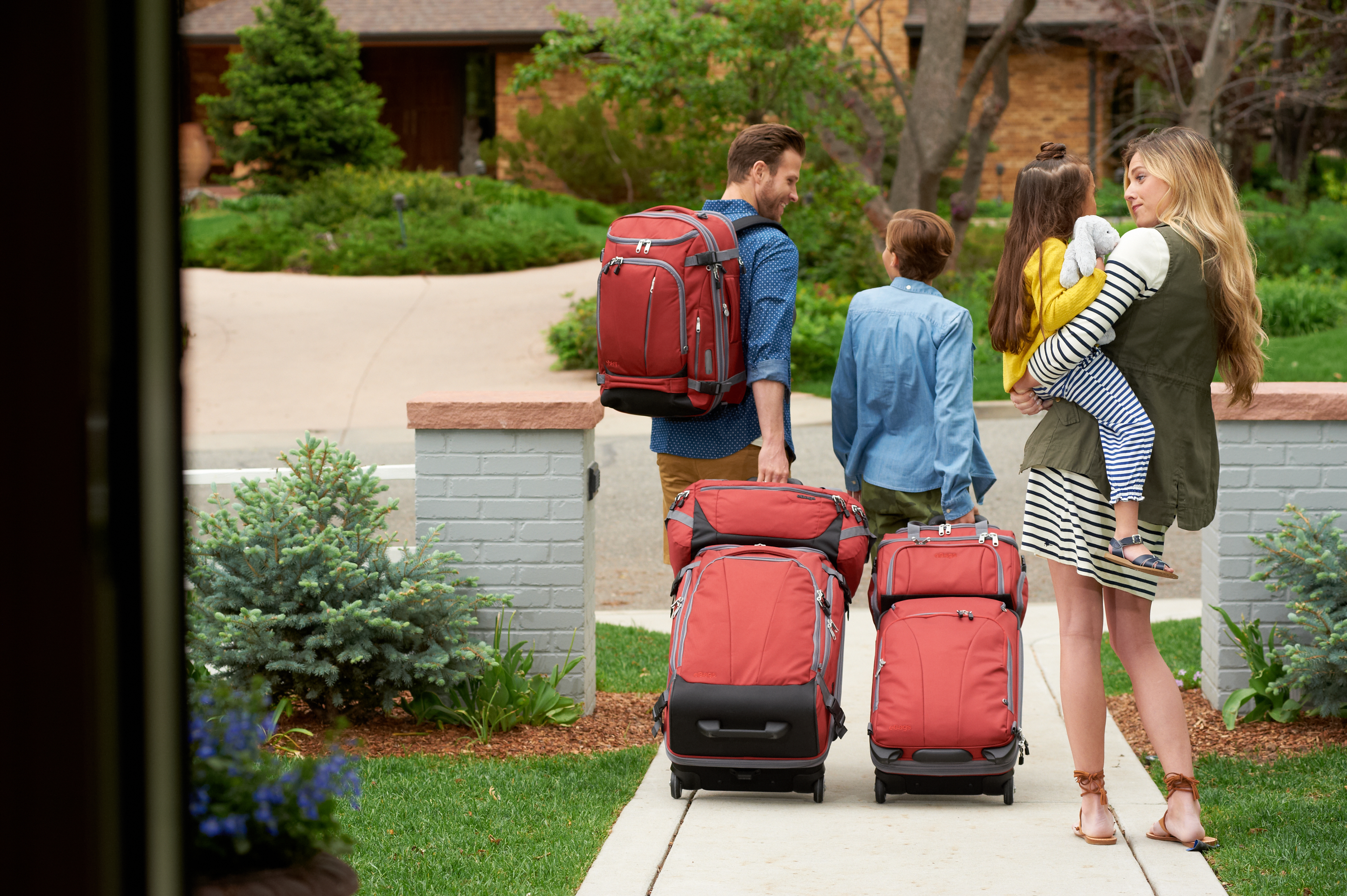 A family of four leaves a rental home, luggage in tow.