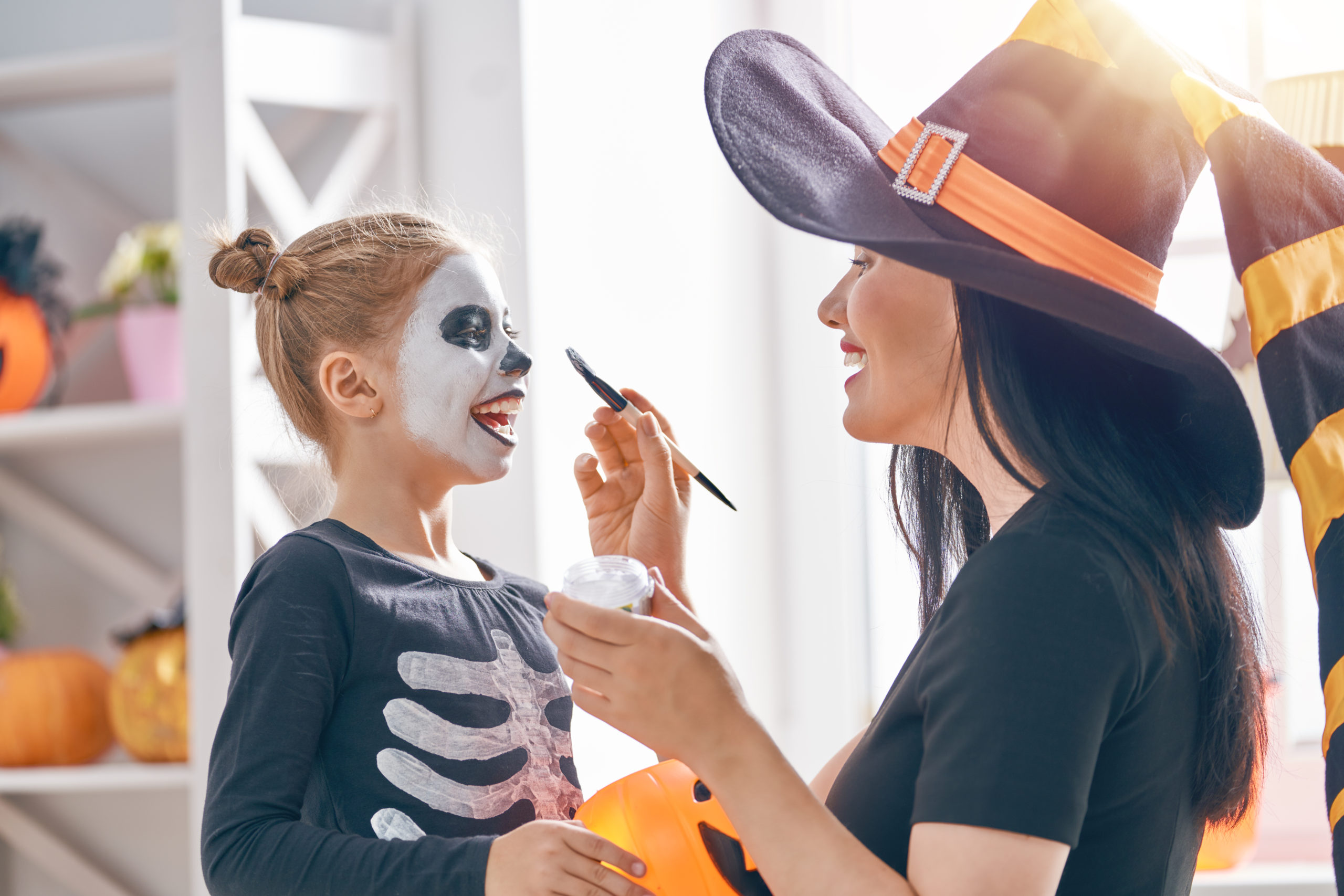 A womanin a witch hat paints a child's face as a skeleton