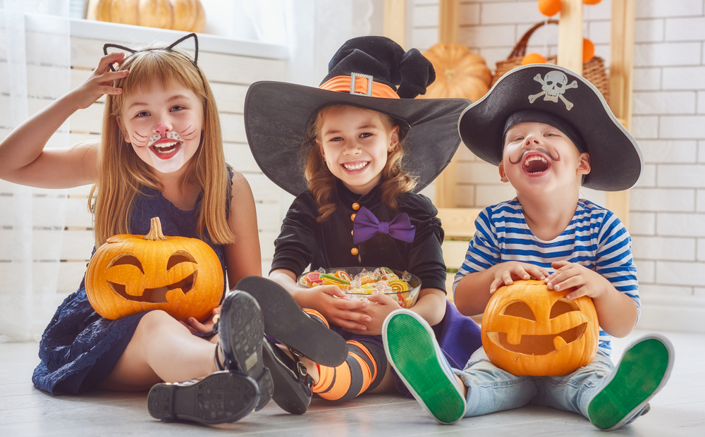 Three children sitting, one is dressed as a cat, one as a witch, and one as a pirate.