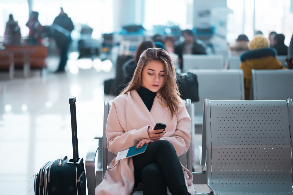 Woman sits waiting at the airport, looking at her phone.