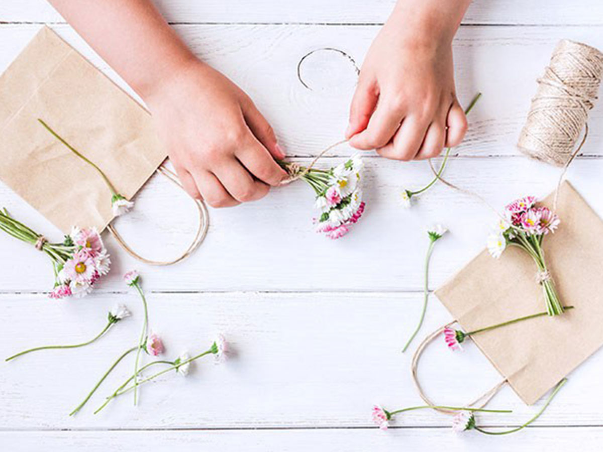 Little hands wrap string around a teeny pink and white bouquet