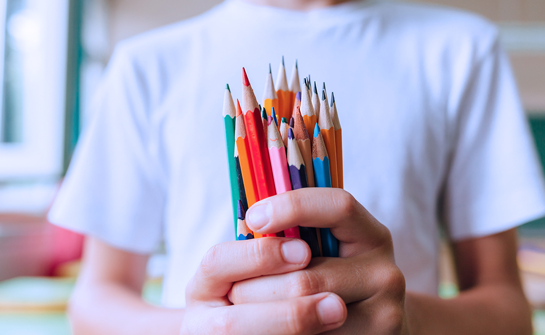 A child holds various colored pencils in their hands