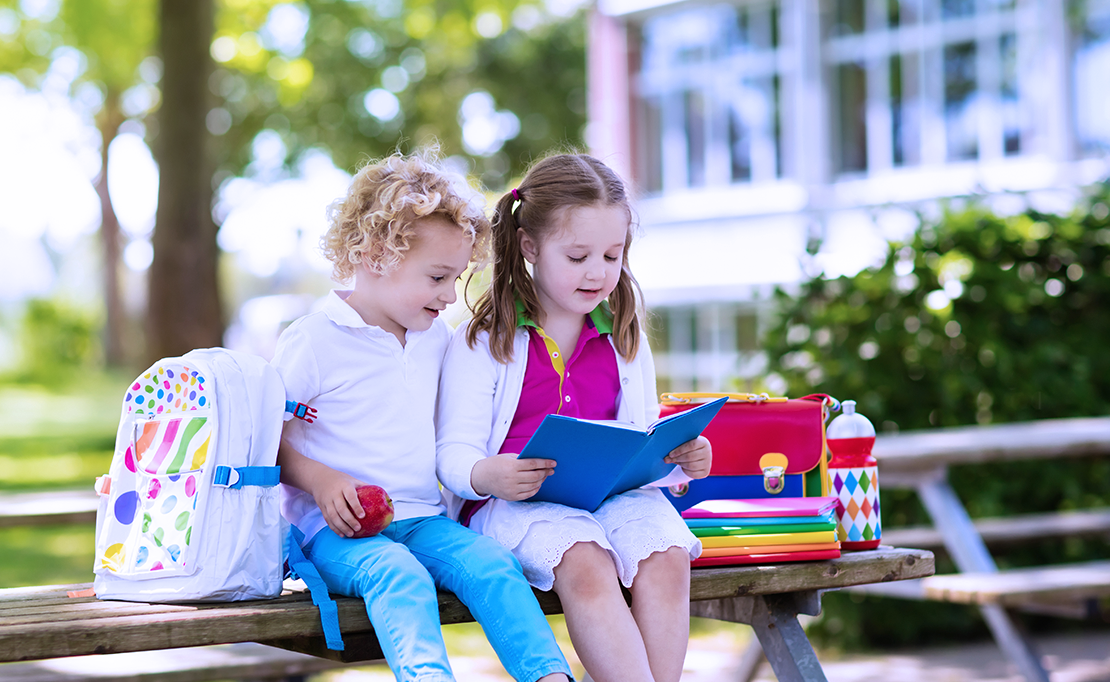School children sit outside on a bench together looking at a notebook