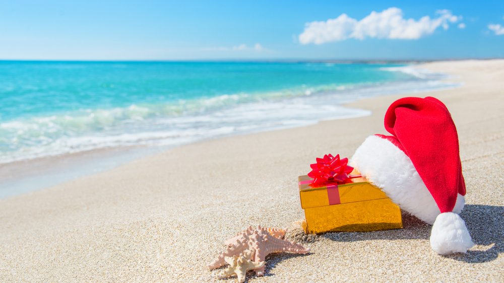 A wrapped gift with a santa hat on it sits on an empty beach