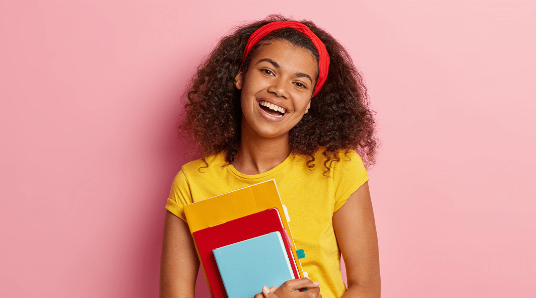 Student smiles with various notebook sizes and colors in hand