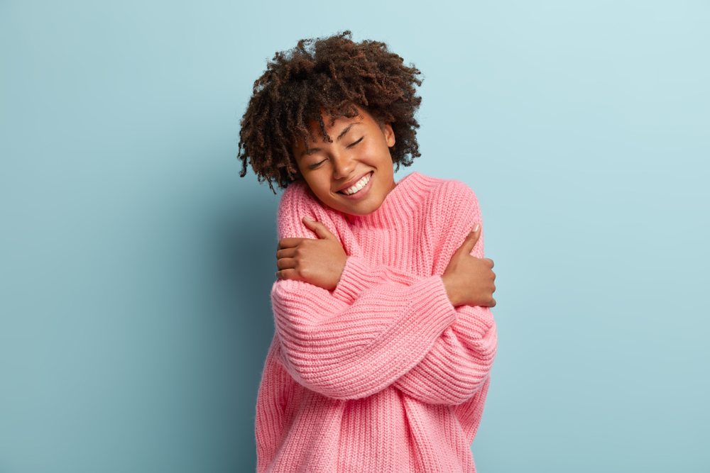 Woman giving herself a big hug in a comfy pink sweater