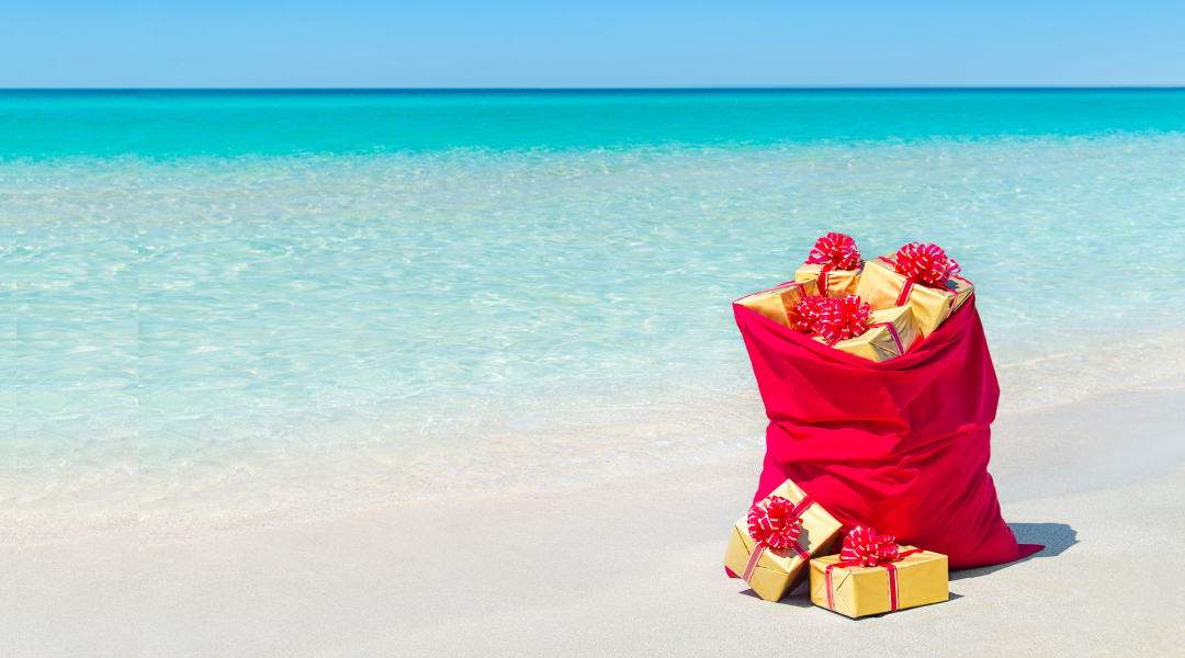 A santa bag full of wrapped presents sits on an empty beach