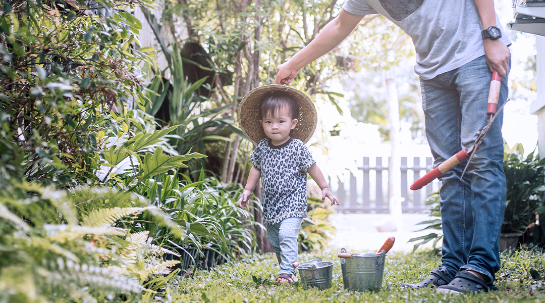 A child wearing a hat gardens in a yard