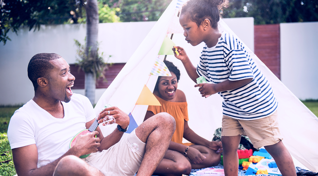 A family plays in a yard with a tent and blowing bubbles