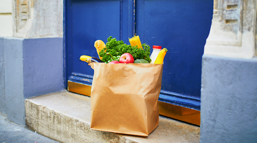 A paper grocery bag full of groceries sits on a doorstep in front of a blue door