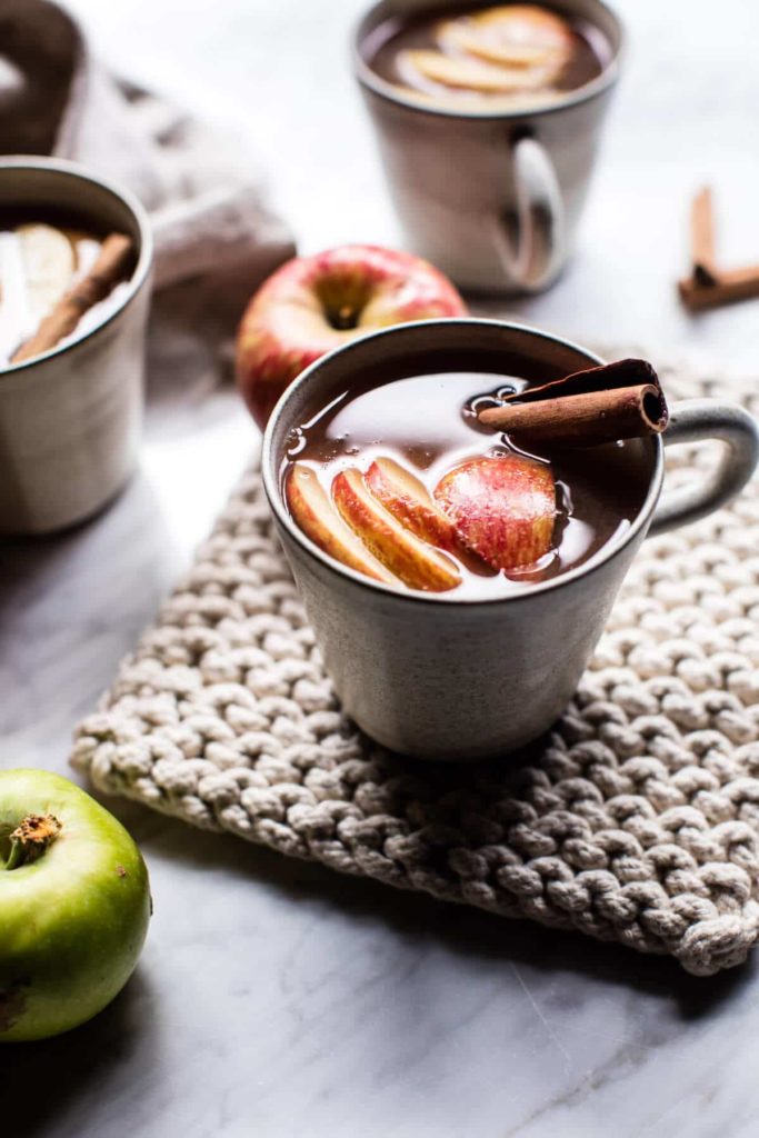 Warm apple cider with sliced red apples and a cinnamon stick in the mug