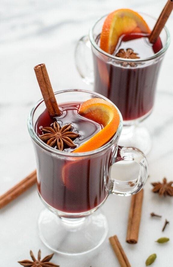 Mulled wine in clear mugs garnished with orange slice, allspice, and a cinnamon stick
