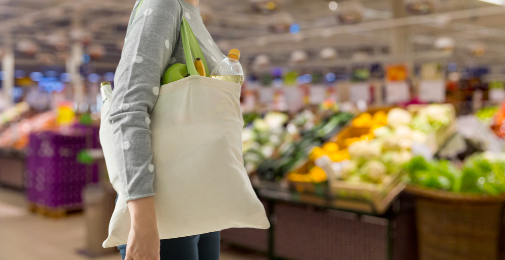 Woman shopping sustainably has a reusable tote bag full of produce.