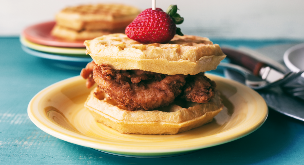 A waffle and fried chicken sandwich with a strawberry on top