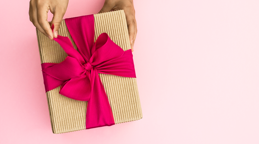 Hands hold a brown wrapped gift with a pink ribbon