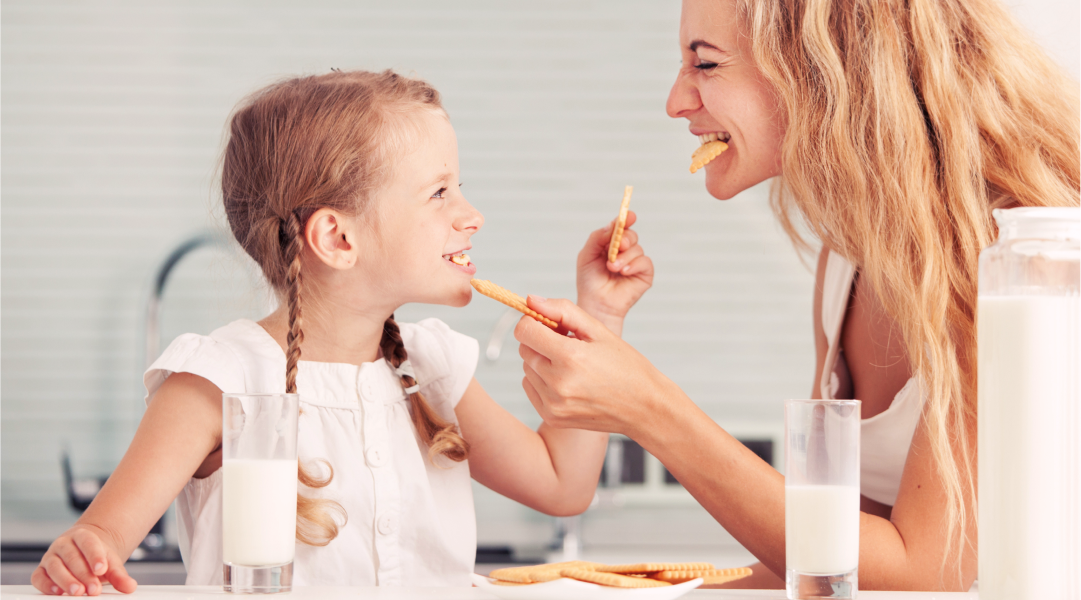 A mother and daughter feed each other cookies while smiling at each other.