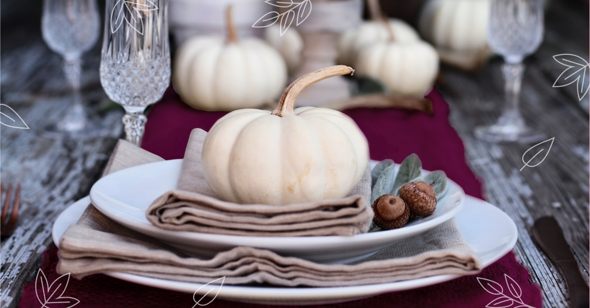 A table set for Thanksgiving with white pumpkins on a plates and a rhubarb colored table runner